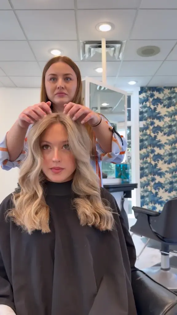 A stylist fluffing a client's fresh blonde balayage waves