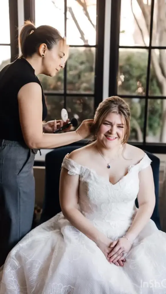 A stylist doing a bride's hair by the window