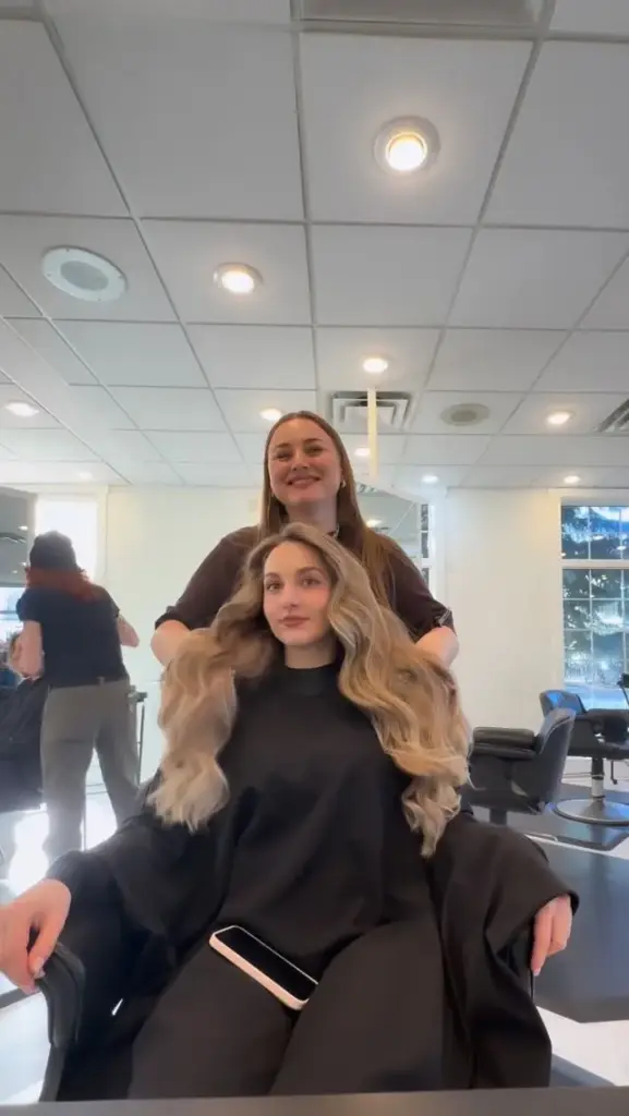 A stylist with a client showing long honey blonde waves