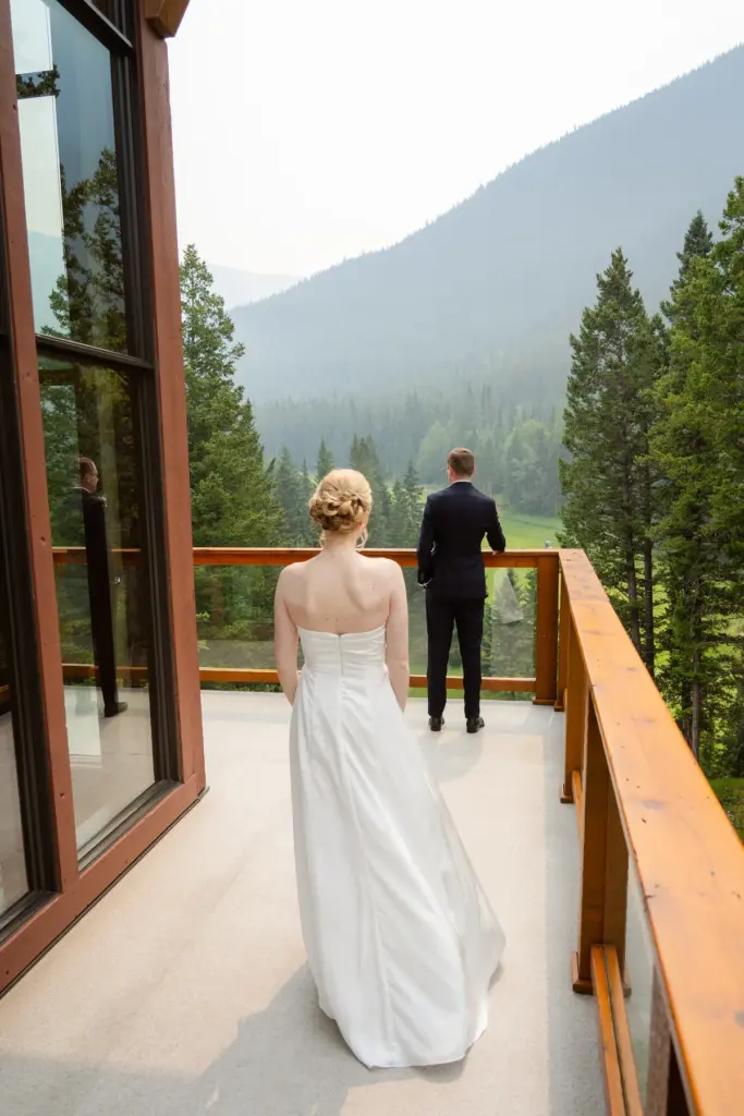 A bride and groom on a deck looking over a forested valley