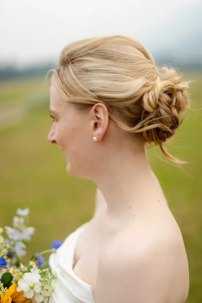 A bride's low textured updo seen in profile, with a wildflower bouquet
